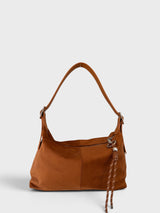 A camel brown faux suede shoulder bag with a matching adjustable strap and a braided tassel detail, shown against a light gray background.