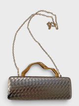 Vegan leather woven-embossed evening clutch in pewter with sculptural gold handle, shown with removable chain strap

