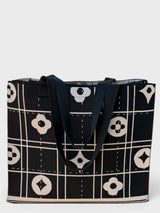 A black tote bag with a cream-colored geometric grid pattern and black shoulder straps, shown against a light gray background.