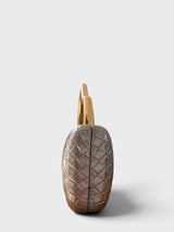 Vegan leather woven-embossed clutch in pewter with sculptural gold top handle shown from a side view
