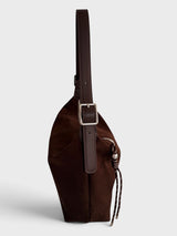 A dark brown faux suede shoulder bag with a wide adjustable shoulder strap and a silver-tone buckle, shown from a side profile view against a light gray background.